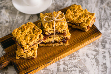 Delicious homemade pie with apple jam. Appetizing slices of grated pie with jam on a wooden board and coffee in a white cup on a light table.