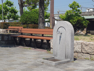 A bench and a water faucet next to it installed in the small garden in front of the local train station.