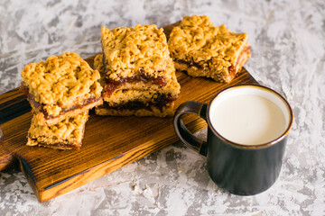 Delicious homemade pie with apple jam. Appetizing slices of grated pie with jam on a wooden board and a cup of milk on a light table.