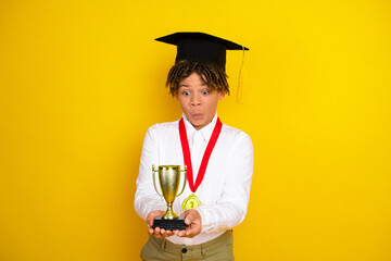 Delighted student holding an award trophy with excitement on a bright yellow background emphasizing...
