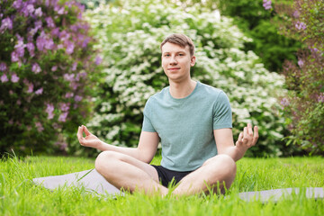 Obraz premium Young man practicing yoga on mat in park