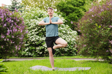 Young man practicing yoga on mat in park