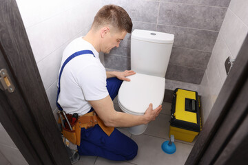 Professional plumber repairing toilet bowl in restroom