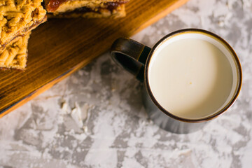 Delicious homemade pie with apple jam. Appetizing slices of grated pie with jam on a wooden board and a cup of milk on a light table.