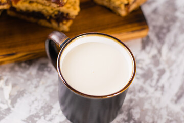 Delicious homemade pie with apple jam. Appetizing slices of grated pie with jam on a wooden board and a cup of milk on a light table.