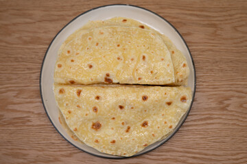Tatar qystybiy bakery. Thinly rolled flatbread showcasing a beautiful golden color and resting on a ceramic plate placed on a wooden table