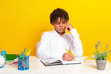 Young schoolboy pondering homework at desk surrounded by colorful stationery in a vibrant yellow...