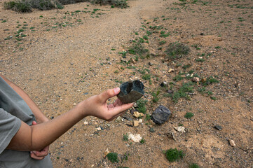A person holding a rock outdoors, Charyn Canyon landscape, nature exploration, geological specimen,...