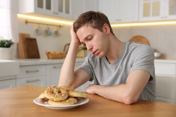 Gluten free diet. Sad woman with pretzels at wooden table in kitchen
