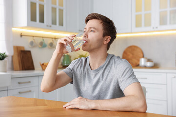 Man drinking water from glass at wooden table in kitchen