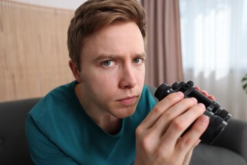 Paranoia. Worried man with binoculars at home