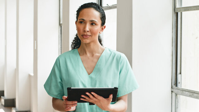 Medical Professional Wearing Scrubs and Using a Digital Tablet in a Bright Hospital Corridor - Powered by Adobe