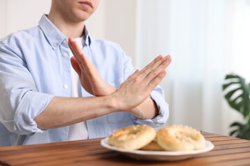 Gluten free diet. Man refusing from pastries at wooden table indoors, closeup