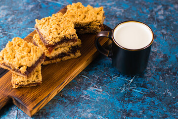 Delicious homemade pie with apple jam. Appetizing slices of grated pie with jam on a wooden board and a cup of milk on the table.