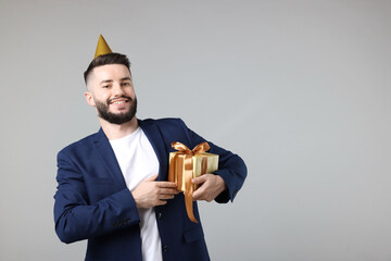 Happy Birthday. Handsome man with party hat and gift box on grey background, space for text