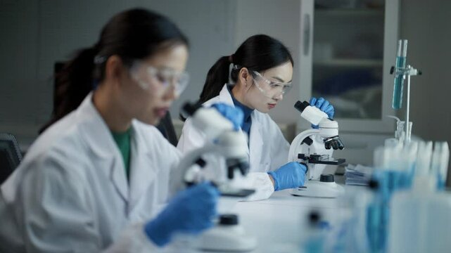 Female scientists using microscopes and performing scientific experiment in a modern laboratory - Powered by Adobe