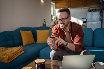 Happy man using credit card and laptop for online shopping at home