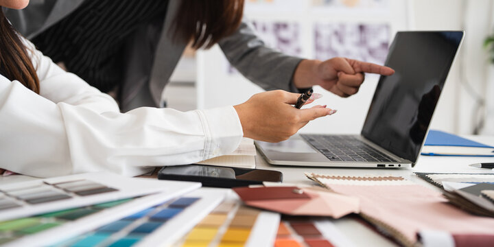 Professional young interior designers and architects working together in the office, they are using a laptop and considering material samples. Close up on hands