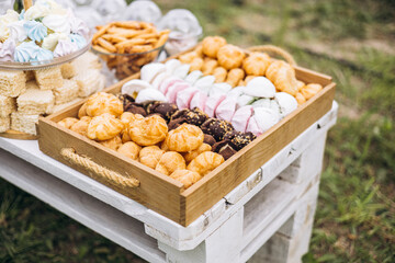 Wooden tray with assorted sweets on table outdoors, picnic dessert composition.