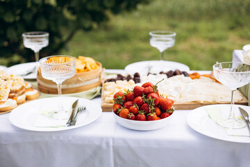 Fresh strawberries on picnic table with toast, cheese, and wildflowers outdoors.