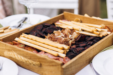 Charcuterie in wooden box with ham and sliced sausage on rustic picnic table.