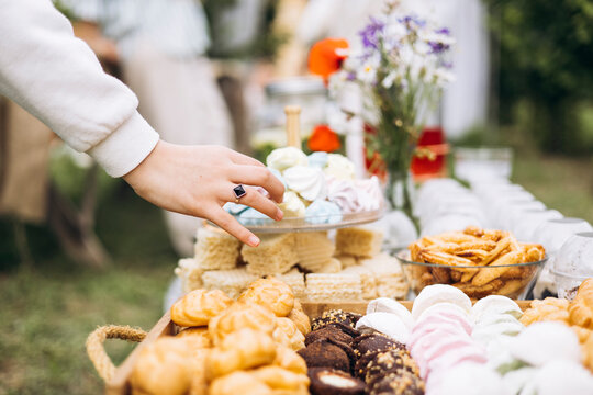 Girl’s hand reaching for sweets on wooden tray outdoors, picnic dessert moment.