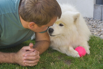 Man lying on grass looking at samoyed dog, concept of pets care, veterinarian, animal friends