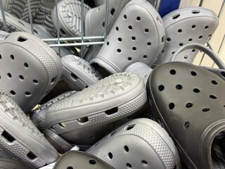 Pile of grey rubber clogs Crocs-style shoes in store basket. Comfortable casual footwear display for everyday use