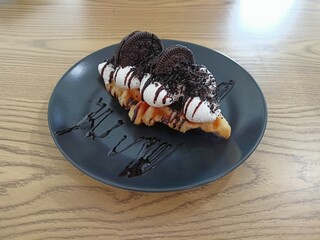 Delicious Waffle Dessert Topped with Whipped Cream, Chocolate Cookies, and Syrup on Black Plate