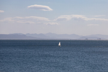 Alone white sailboat in the middle of the blue sea against the silhouette of mountains