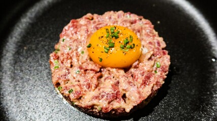 close up of raw egg and tuna tartar in a round shape on a black plate