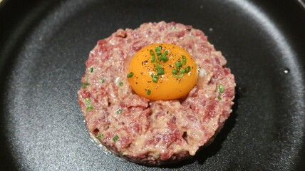 close up of raw egg and tuna tartar in a round shape on a black plate