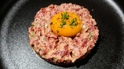 close up of raw egg and tuna tartar in a round shape on a black plate