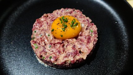 close up of raw egg and tuna tartar in a round shape on a black plate