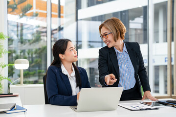 Two business women sit at desk discuss project details, diverse female colleagues met in office,...