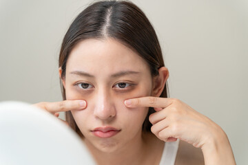 Bored, insomnia asian young woman, girl looking at mirror hand touching under eyes with problem of...