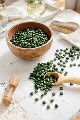 Organic green spirulina pellets in a wooden bowl with scattered pieces on a rustic table. Concept of homeopathy and alternative medicine 