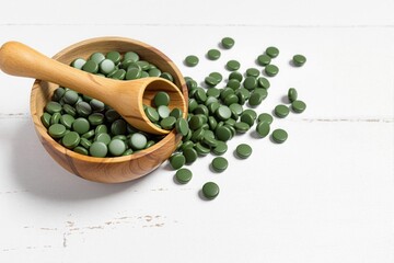 Spirulina, Green health supplement tablets in a wooden bowl a white background with copy space 