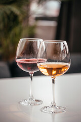 Two elegant wine glasses filled with red and amber wine stand on a white surface, reflecting soft indoor light in a cozy setting