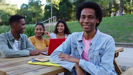Portrait of young Latin American Gen Z non binary student person smiling at camera sitting together with diverse classmates working on laptop at college campus. Diversity and education concept. - Powered by Adobe