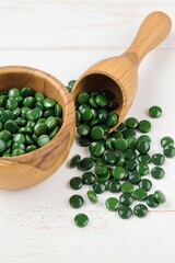 Spirulina, Green circular tablets spill in wooden bowl on light surface, natural supplement and healthy lifestyle choices
