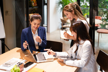 Confident mature business professional woman talking to younger female colleague at office table,...