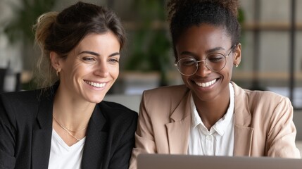 Two women collaborating on a laptop in a modern office, smiling and engaged in discussion