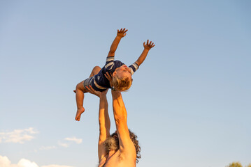 Man holding his son in his arms, lifting him up in the air, son having a sense of security, trust in his father, family enjoying together on a sunny day, sense of freedom, security, protection, safety