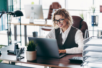 Confident businesswoman working on a laptop in her modern office with professional enthusiasm and...