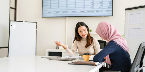 Attractive and friendly young Asian businesswoman training and giving an advice to her Muslim colleague in the office.