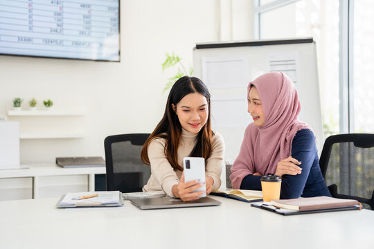 Happy diverse colleagues browsing social media content during working day in office. female partners discussing cellular application while connecting to internet