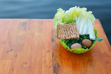 Organic vegetables, eggs, instant noodles are arranged in green plastic basket ready for meal. Boil...