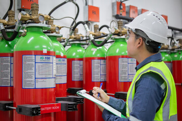 Worker wearing helmet and safety vest performs gas inspection on fire protection equipment in...