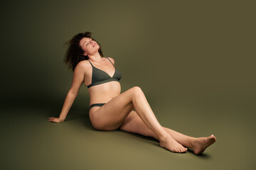 Confident Young Woman in Stylish Lingerie Showcasing Body Positivity on a Minimalistic Khaki...
